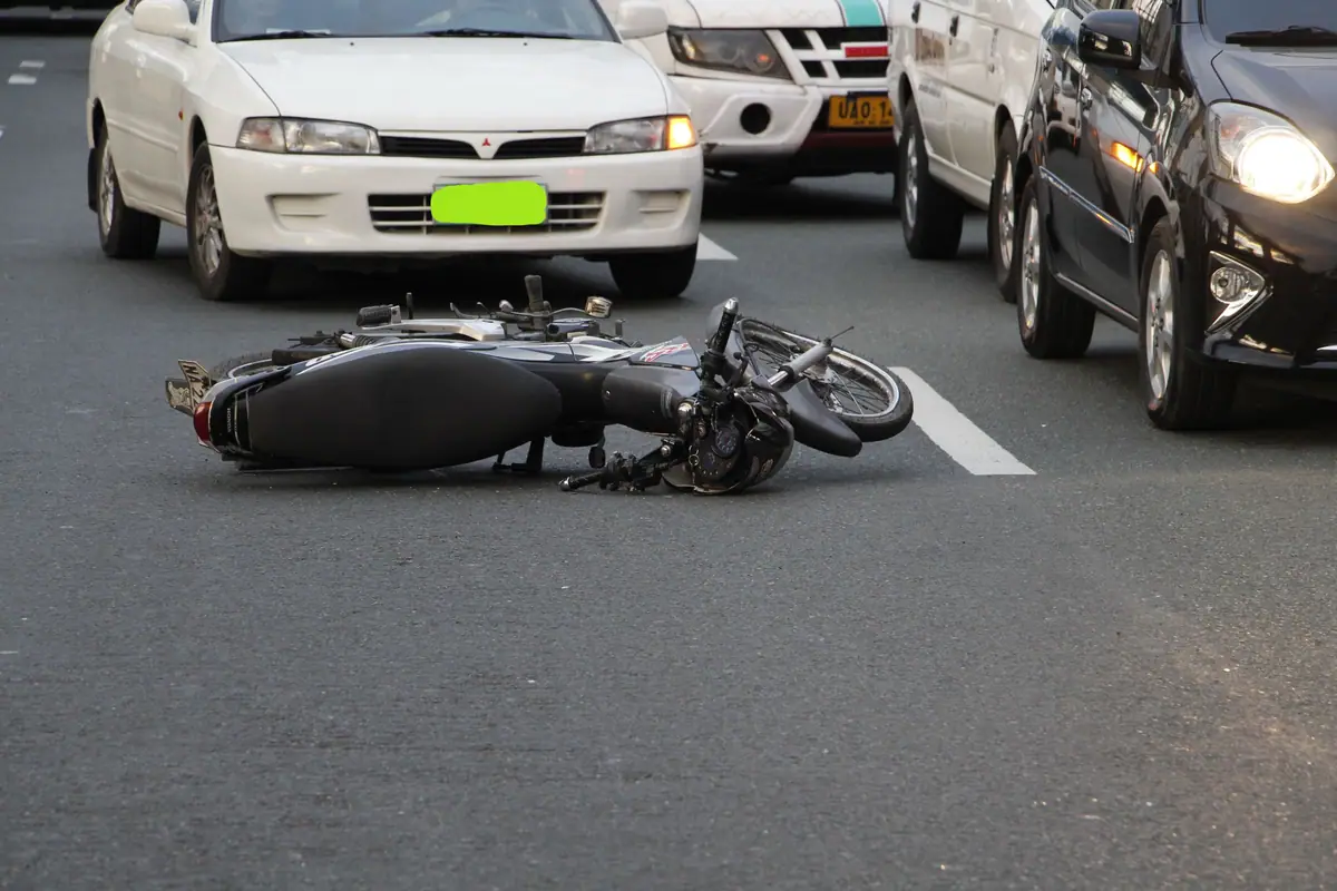 A motorbike lying on the road after a crash, cars stopped around it
