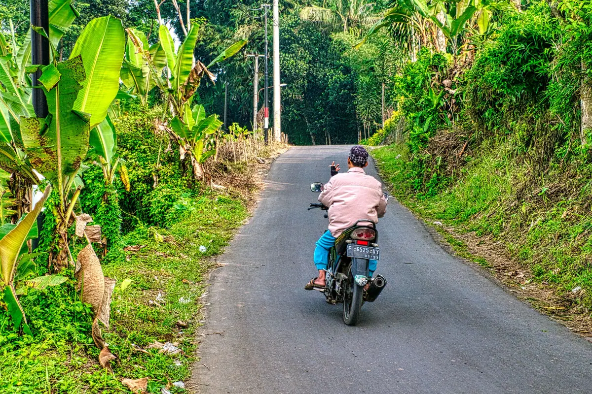 A motorcyclist on a narrow road between green hills