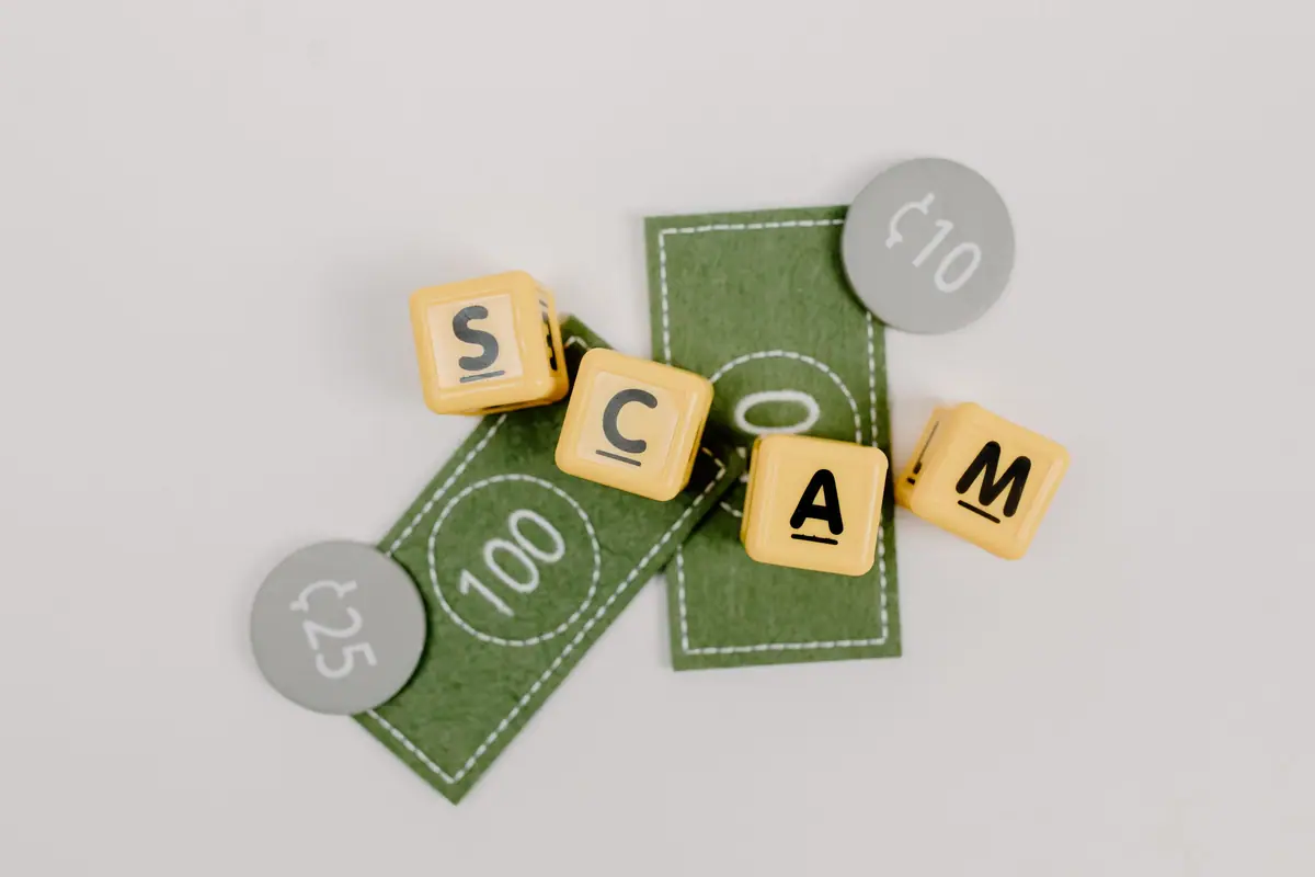Letter tiles spelling SCAM on play money