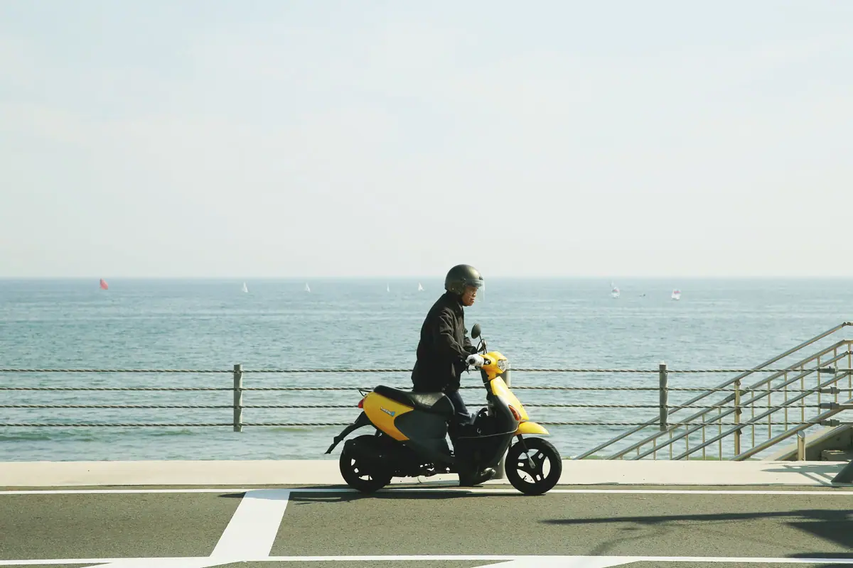 A rider on a yellow scooter on a seaside road