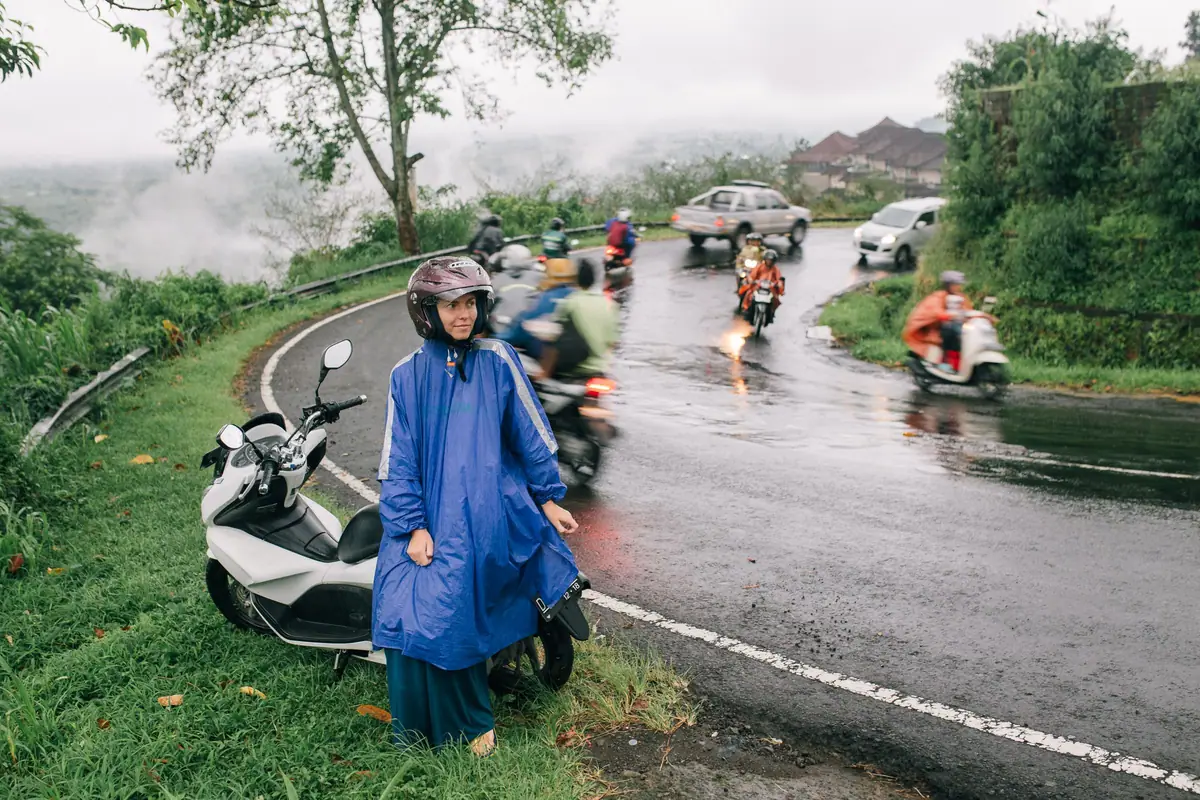 Scooter riders in raincoats on a wet road winding through hills