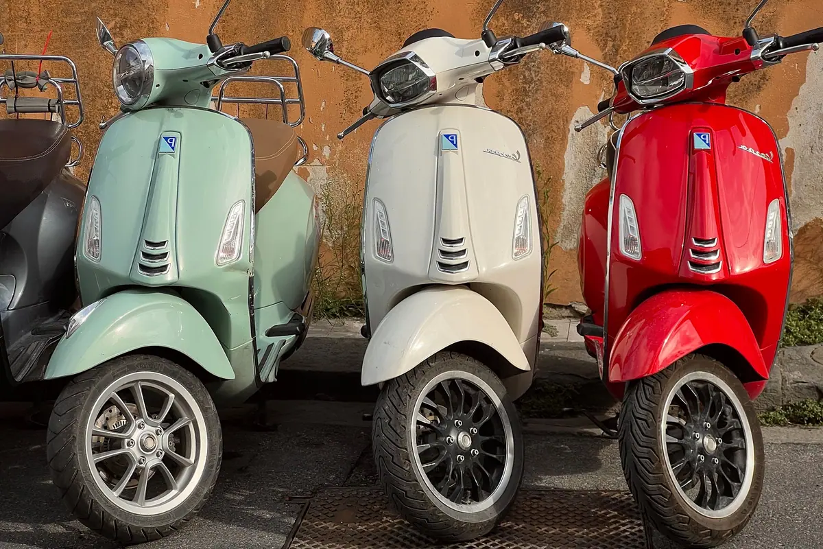 Three vintage scooters parked against an old wall